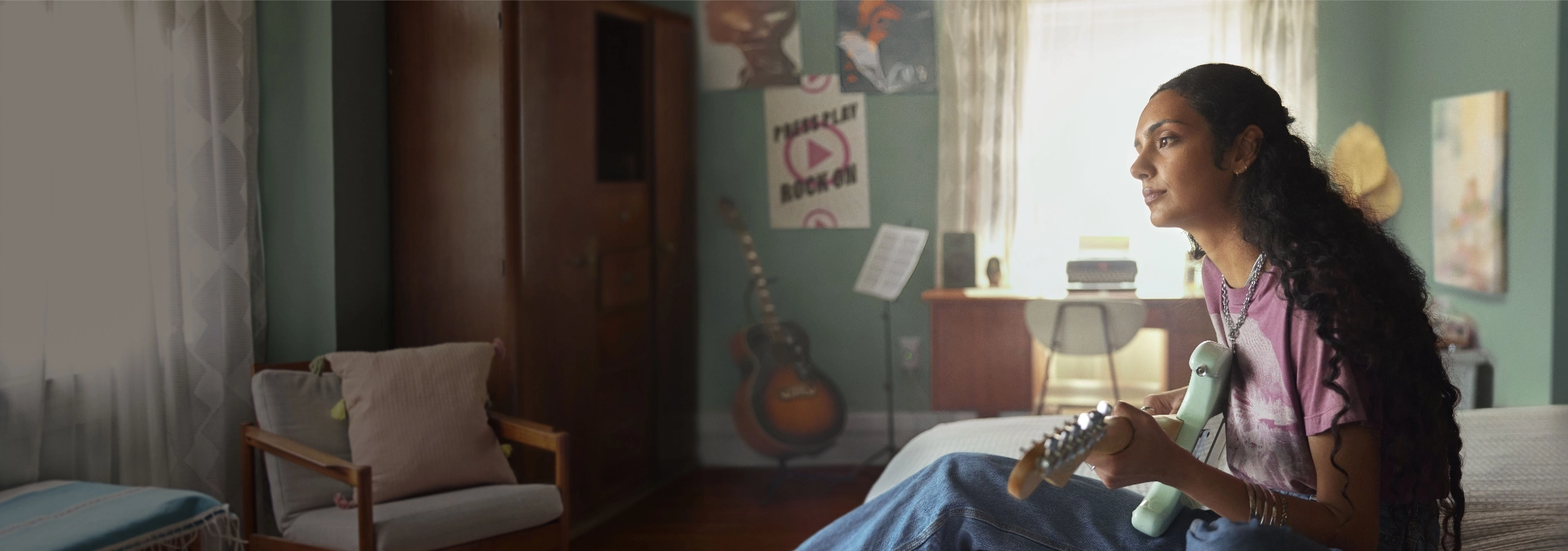 Woman sitting on the edge of a bed playing guitar